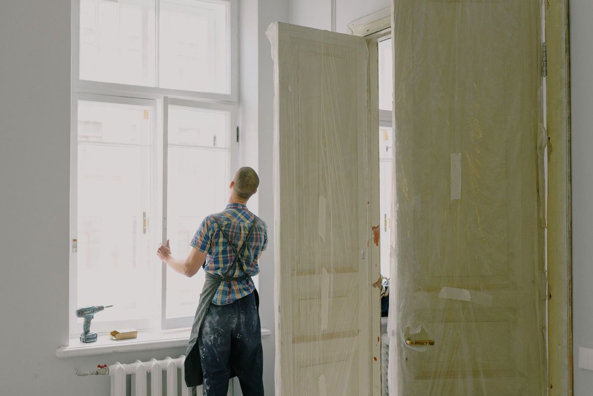 Vakman stelt een nieuw wit raam af in een kamer in renovatie, naast nieuwe binnendeuren